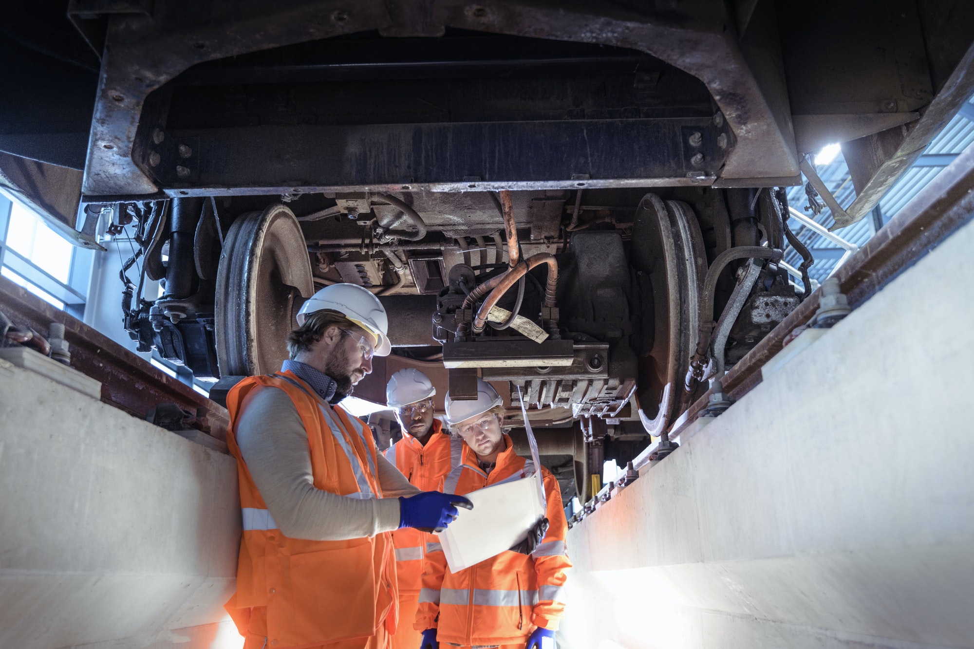 Instructor and apprentices under train in railway engineering facility